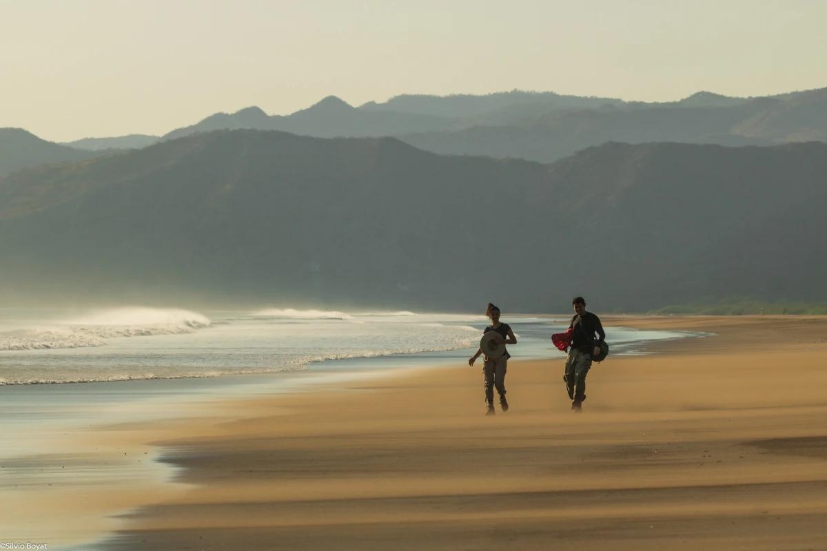 Two travelers walking in the wind sweeping the wild Naranjo beach in Santa Rosa National Park